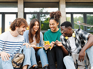 Junge Menschen sitzen beieinander und nutzen mobile Endgeräte.