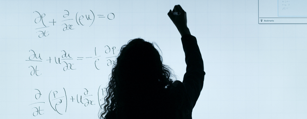 Eine Frau rechnet eine komplexe Formel an einer durchsichtigen Tafel.