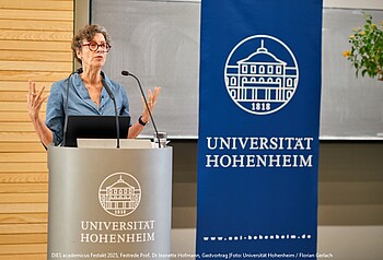 Foto: Eine Person steht an einem Rednerpult mit dem Logo der Universität Hohenheim. Im Hintergrund ist ein blaues Banner mit dem Schriftzug "UNIVERSITÄT HOHENHEIM" und einem Gebäude-Emblem zu sehen. Text am unteren Rand: "DIES academicus Festakt 2025, Festrede Prof. Dr. Jeanette Hofmann."