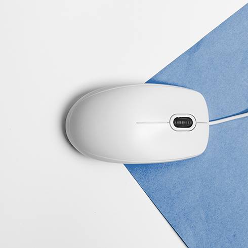 Draufsiht auf eine weiße, kabelgebundene Computermaus, die auf einem blaufarbenen Papier auf einem weißen Untergrund steht.